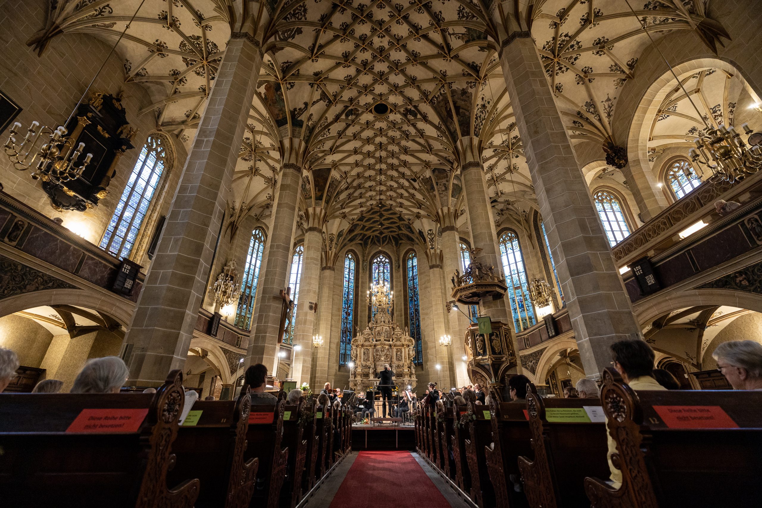 Das Innere einer Kirche mit Zuschauern auf den Bänken und einem Orchester vor dem Altar.