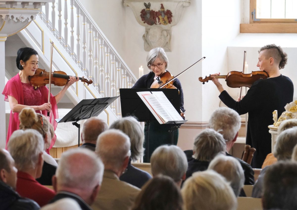 Drei Frauen spielen in einer Kirche auf ihren Streichinstrumenten vor Publikum.